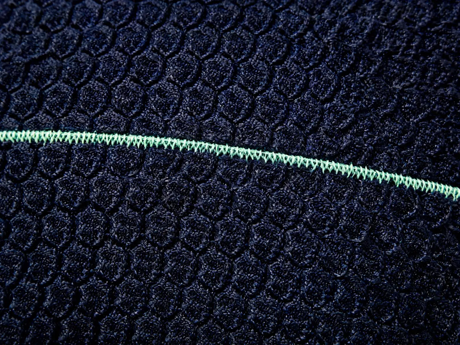 Macro view of navy 3D honeycomb compression knit with a mint accent seam